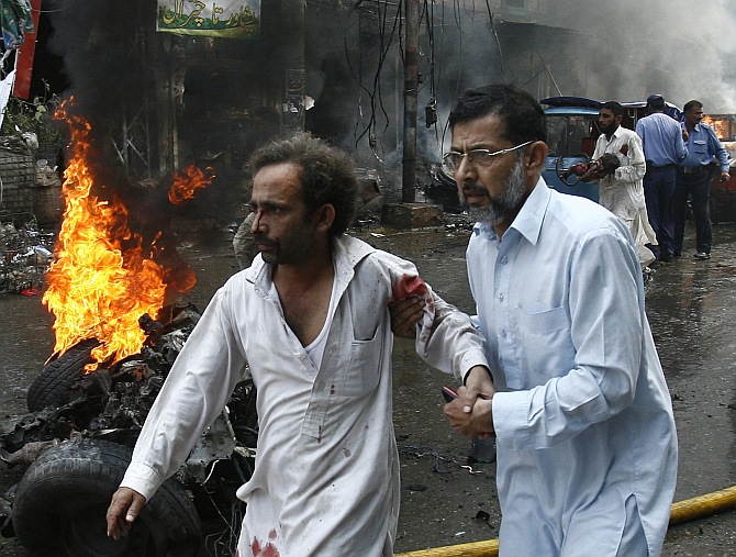 A man helps an injured man walk away from the site of a bomb attack in Peshawar