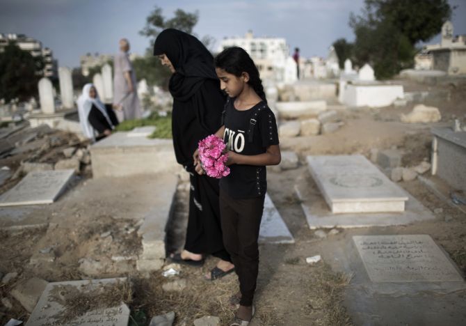 A Palestinian woman and girl carry flowers to a family grave at a cemetery in Gaza City.