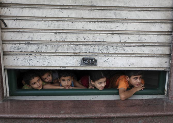 Palestinian children look through a store shutter at ambulances transporting casualties during Israeli offensive in Gaza City.