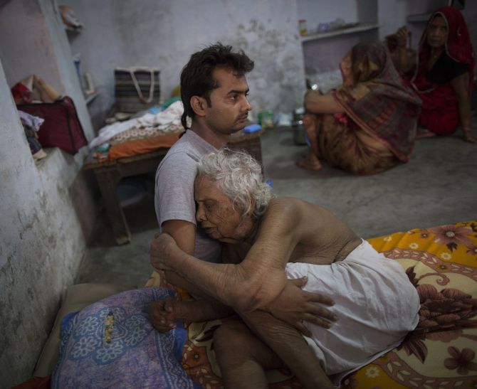 Bhogla Devi, 97, is comforted by her grandson Divyesh Tiwari as she cries in pain at Mukti Bhawan.