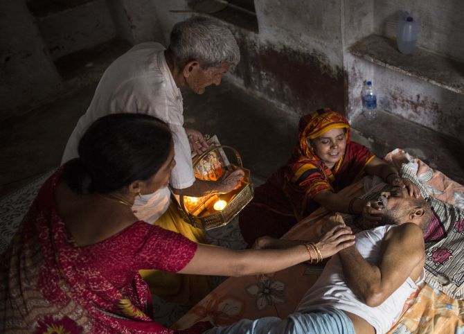 Kishore Pandey, 82, lies on a bed as his daughter, Usha Tiwari, holds him and a priest stands by them.