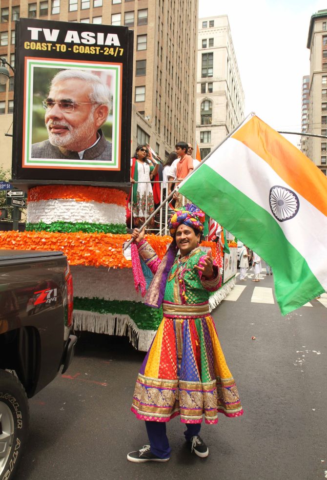A man dressed in traditional Indian clothes waves the Indian flag as a flotilla with the picture of Indian Prime Minister Narendra Modi is behind him. 