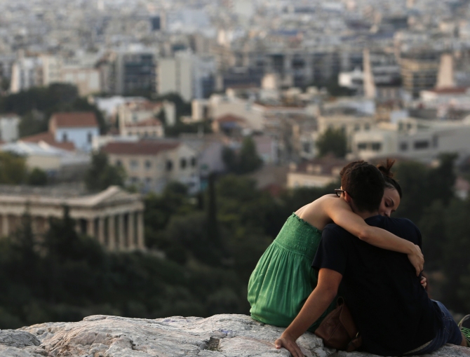 A couple embraces as they sit on a hill overlooking Athens near the archaeological site of the Acropolis in Athens.