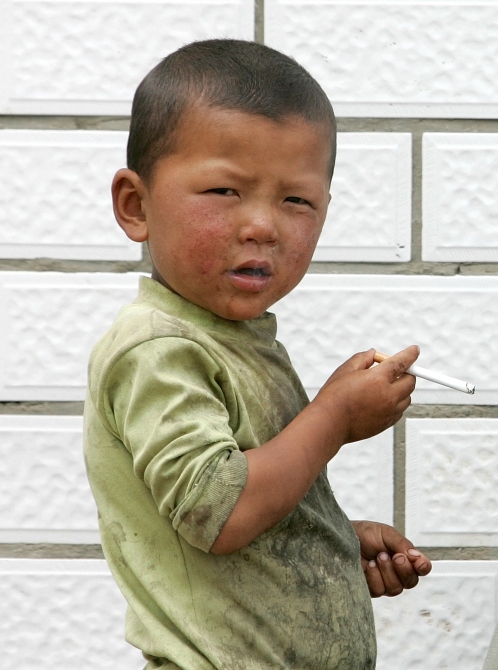 An ethnic Tibetan boy smokes a cigarette, which he had asked from a man (not pictured), at Sangke grassland in Xiahe, western China's Gansu province.
