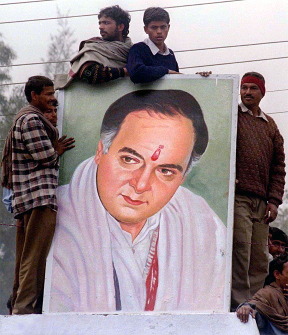 People gather around a poster of Rajiv Gandhi at an election rally