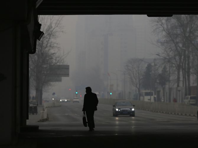 A man is silhouetted against the haze sky as he walks underneath an overpass and a car uses a light in the daytime amid the heavy haze in Beijing.