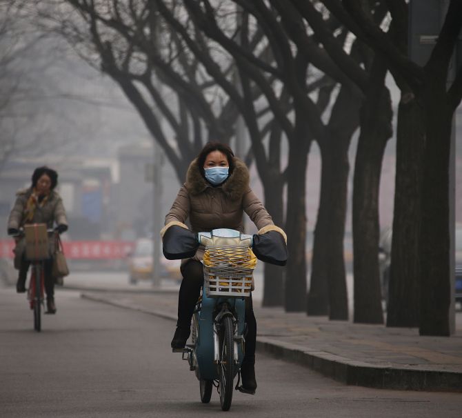 A woman wearing a mask rides an electric bicycle along a street on a hazy afternoon in Beijing on Monday. 
