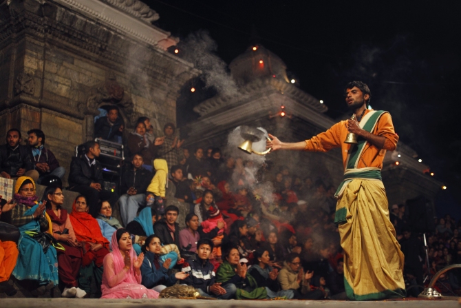 A priest offers an evening prayer as devotees sing holy songs on the eve of Shivaratri festival at the premises of a temple.