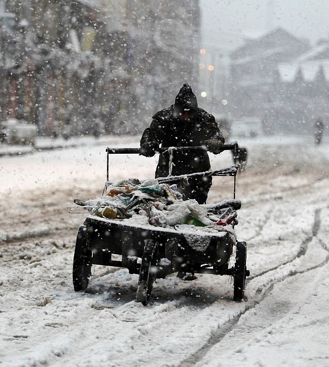 A man pushes his handcart through a snow-covered street during snowfall on a cold winter morning in Srinagar