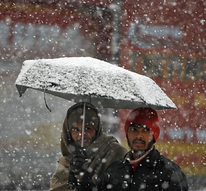 Men walk under an umbrella during snowfall on a cold winter morning in Srinagar