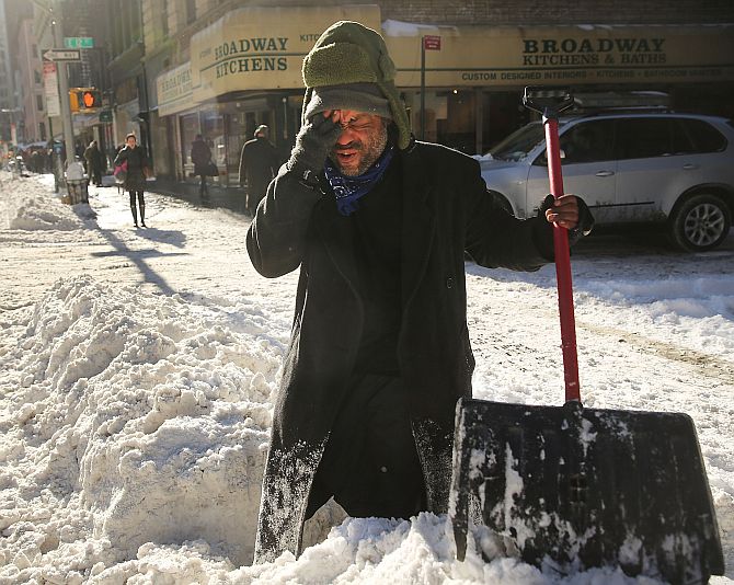 Diego Ramos, who is homeless and lives under nearby building scaffolding, pauses as he clears a sidewalk of snow in lower Manhattan following a snow storm that left up to eight inches of snow