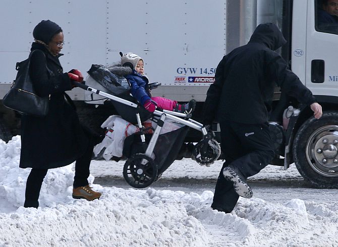 A man helps a woman carry a child in a stroller through a snow covered crosswalk in midtown Manhattan in New York City