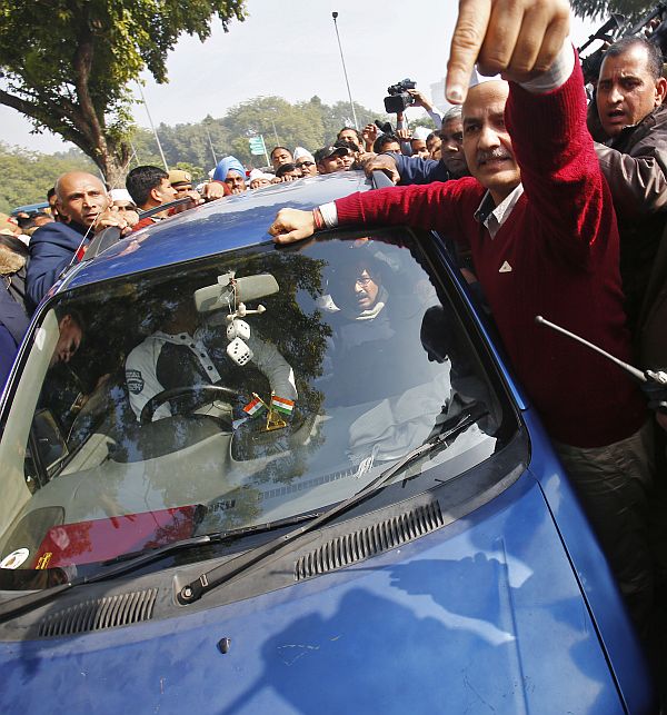 AAP leader Manish Sisodia (in red) gestures near the car carrying Delhi Chief Minister Arvind Kejriwal