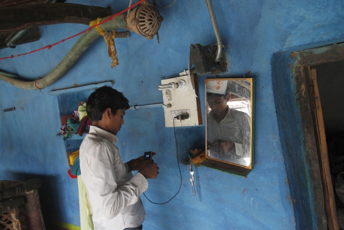 A boy charges his mobile phone from an electric board powered by solar energy inside his house at Meerwada village of Guna district in Madhya Pradesh.