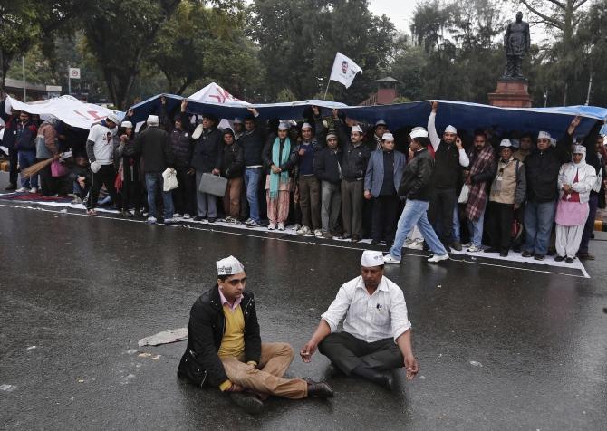 Supporters of the Aam Aadmi Party take part in a sit-in protest as others use a sheet to protect themselves from the rain in New Delhi