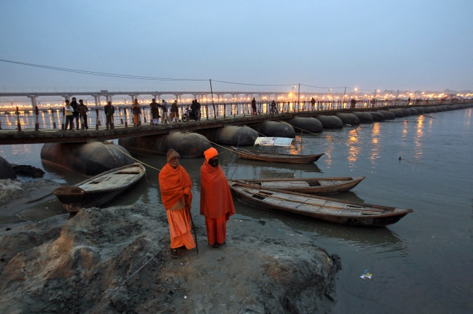 Sadhus or Hindu holy men stand on the banks of river Ganges next to a pontoon bridge in Allahabad
