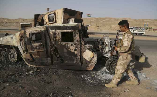 A Kurdish soldier walks past an Iraqi army vehicle destroyed by ISIS fighters