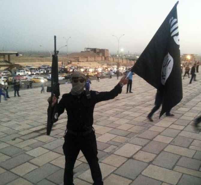 An ISIS fighter holds an flag and a weapon on a street in Mosul, Iraq
