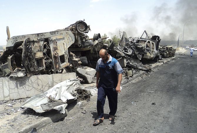 A man walks past cars, which have been reduced to debris owing to the terror activities of the Sunni rebels.