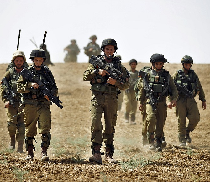Israeli soldiers from the Nahal Infantry Brigade walk across a field near central Gaza Strip July 12