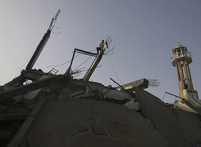 A youth puts up a Palestinian flag over the rubble of a mosque, which police said was destroyed in an Israeli air strike, in Nuseirat in the central Gaza Strip