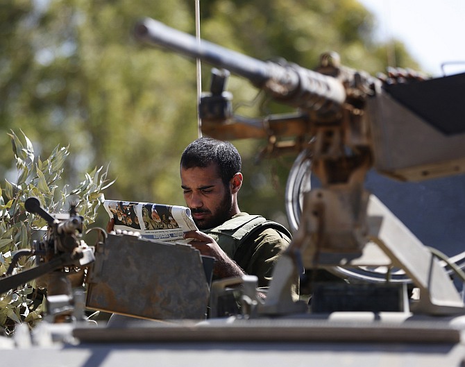 An Israeli Army reservist reads a newspaper as he sits atop an armoured personnel carrier (APC) outside the central Gaza Strip