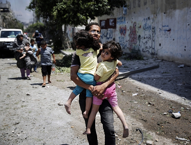 A Palestinian man carries children in the Shejaia neighbourhood, which was heavily shelled by Israel during fighting, in Gaza City 