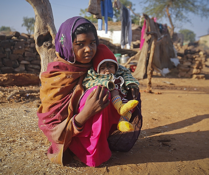 Krishna, 14, sits with her four-month-old baby Alok, outside her house in a village near Baran, Rajasthan