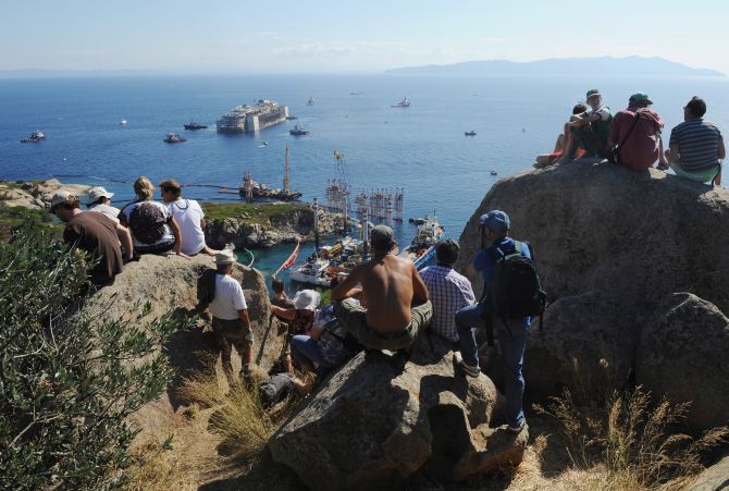People watch as the wrecked cruise ship Costa Concordia is towed by tugs from Giglio after being refloated. 