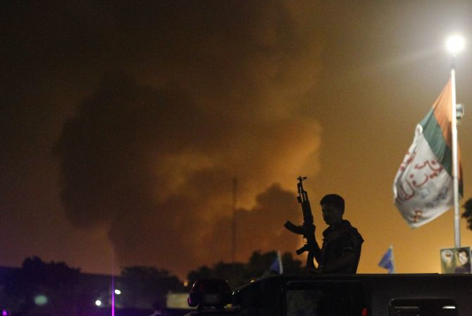 A gunman stands guard as smoke billows from Jinnah International airport.