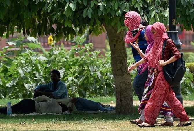 Students walking with their heads covered while others take rest under a tree on a hot day in Delhi