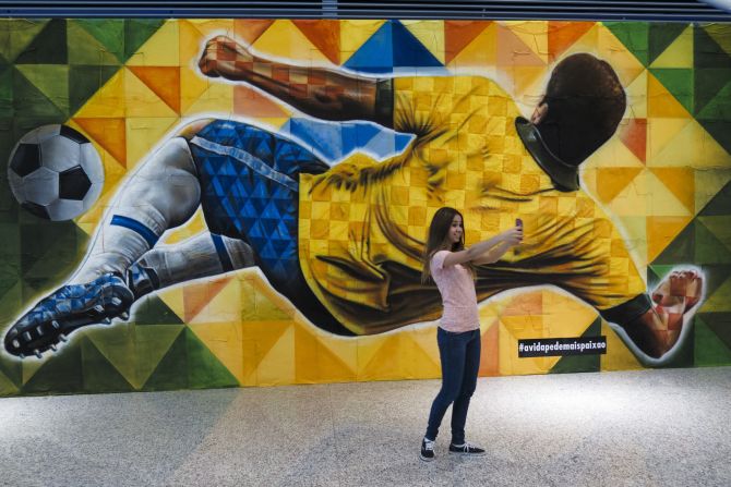 A girl takes a selfie before a mural depicting a player kicking the ball.