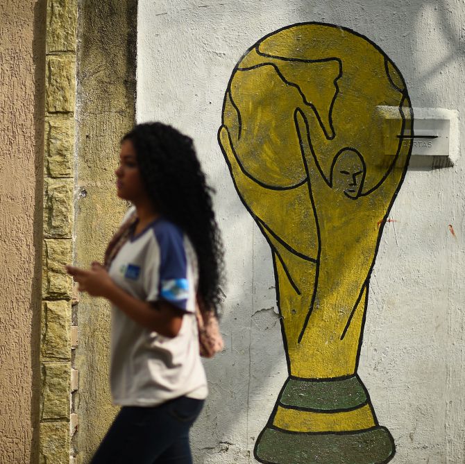 A girl walks past a mural depicting the World Cup trophy on the streets of Brazil.