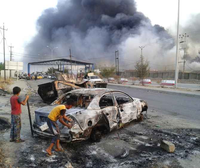 Children stand next to a burnt vehicle during clashes between Iraqi security forces and al Qaeda-linked militants in Mosul