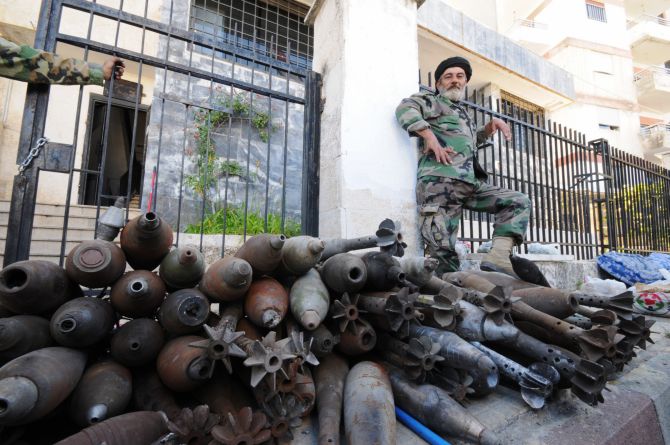A soldier loyal to Syrian President Bashar al-Assad poses next to mortar bombs that rebels left behind, at the Armenian Christian town of Kasab