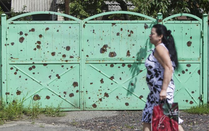 A woman walks past a gate filled with shrapnel holes, in the eastern Ukranian city of Slaviansk