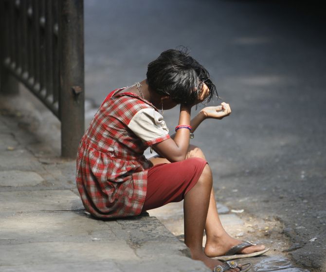 A small girl sits on a Mumbai road with her hand out begging for alms