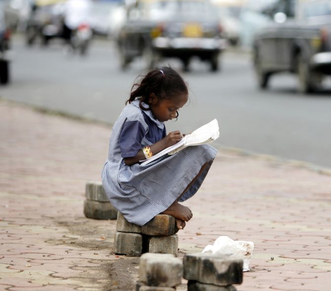 A girl belonging to a homeless family, studies school books at a pavement in Mumbai 