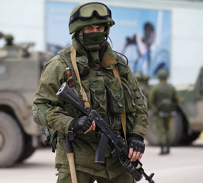 An armed servicemen patrols near Russian army vehicles outside a Ukrainian border guard post in the Crimean town of Balaclava