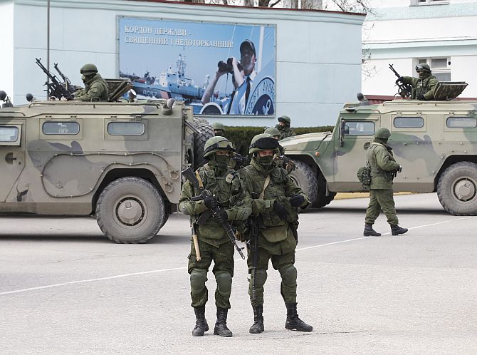 Armed servicemen wait near Russian army vehicles outside a Ukranian border guard post in the Crimean town of Balaclava