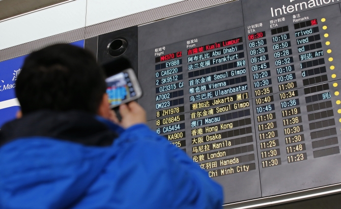   A man takes pictures of a flight information board displaying the Scheduled Time of Arrival of Malaysia Airlines flight MH370 (top, in red) at the Beijing Capital International Airport 