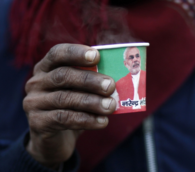 A man holds a paper cup carrying a portrait of at a tea stall in the old quarters of Delhi.