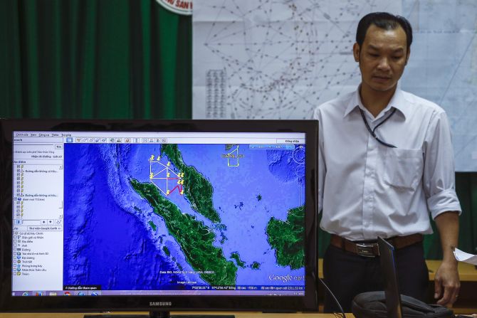 A Vietnamese officer stands next to a TV screen showing a flight route during a news conference about their mission to find missing Malaysia Airlines flight 