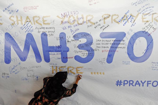 A woman writes a message of support and hope for the passengers of the missing MH370 on a banner at the Kuala Lumpur International Airport 