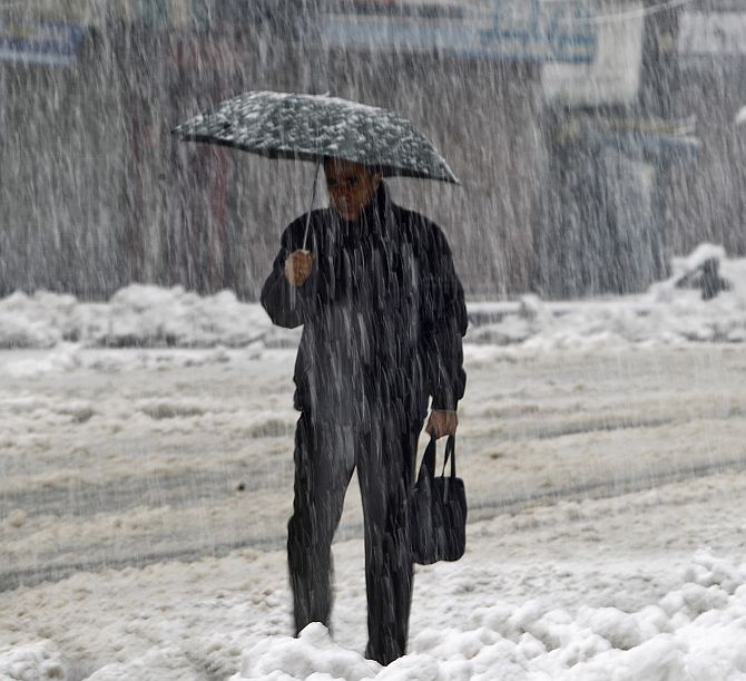 A man holds an umbrella as he walks on a road during heavy snowfall in Srinagar