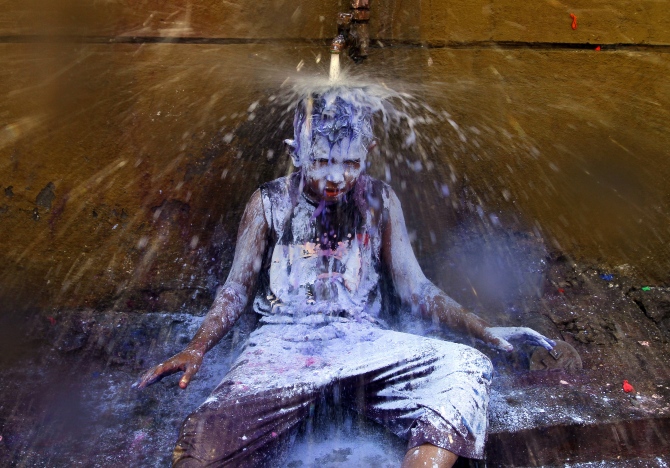 A boy sits under a water tap to wash himself after taking part in Holi celebrations in Chennai.