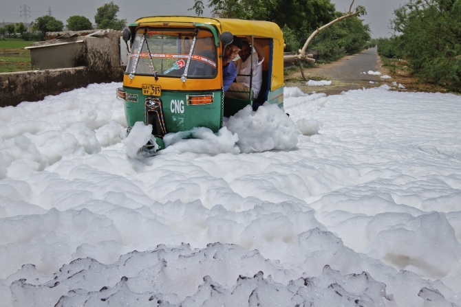 A man looks out of his auto rickshaw as he drives through foam overflowing from a drain outside a factory, in Ahmedabad.