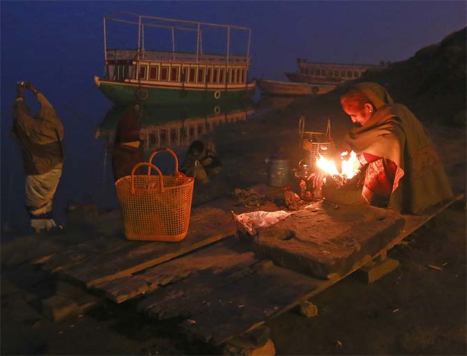 A devotee warms herself around a fire as others pray at dawn on the banks of Ganga in Varanasi