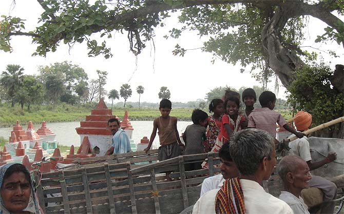 Children on a bullock cart pass by the school area in Gandaman.