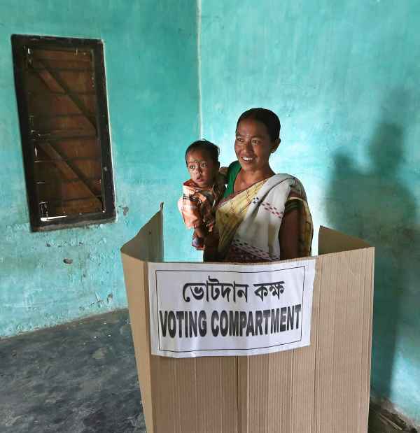 A woman holds her son as she casts her vote inside a polling booth at Majuli, Assam during the 2014 Lok Sabha elections